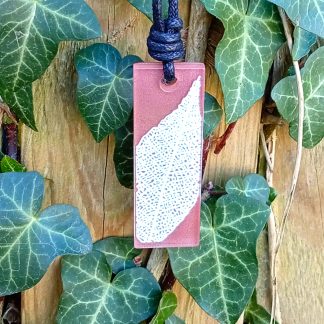 Warm brown rectangular pendant with cream leaf skeleton design against ivy covered wood in natural daylight